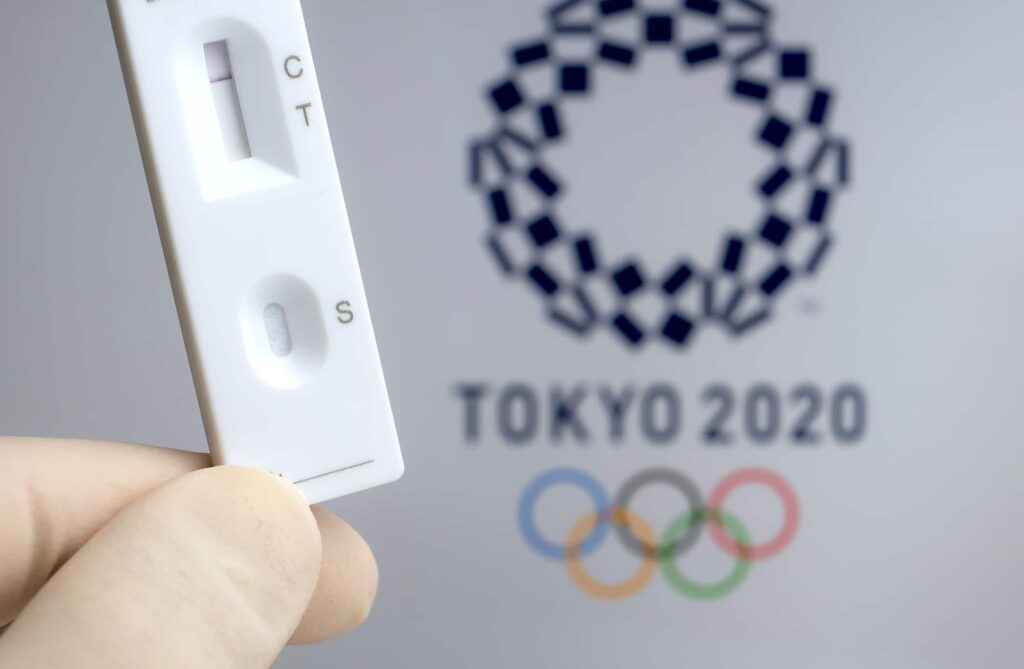 Negative PCR test in front and blurred Tokyo 2020 logo on the blurred background. Concept for Tokyo COVID Olympic games in 2021. Stafford, United Kingdom, June 1, 2021.